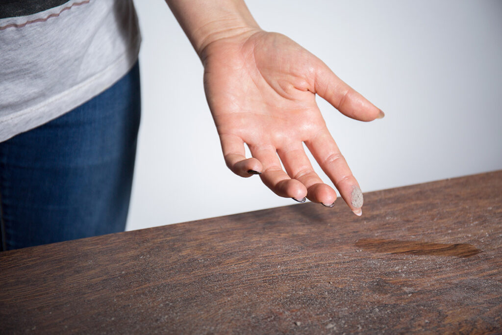 A hand showing dust wiped from a table