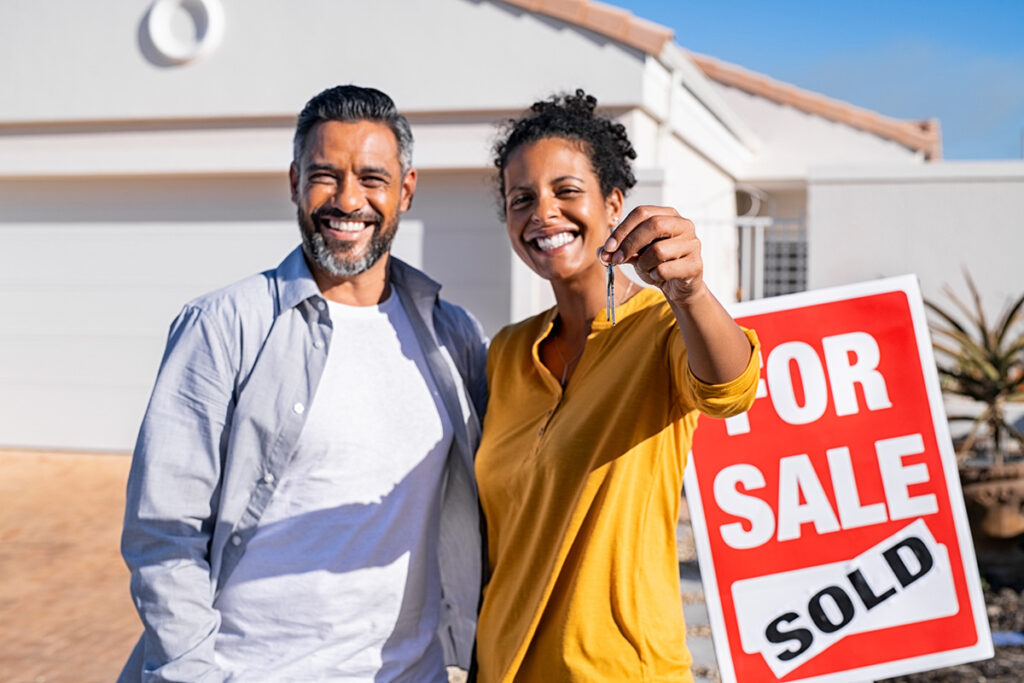 A man and woman outside a sold home holding out keys