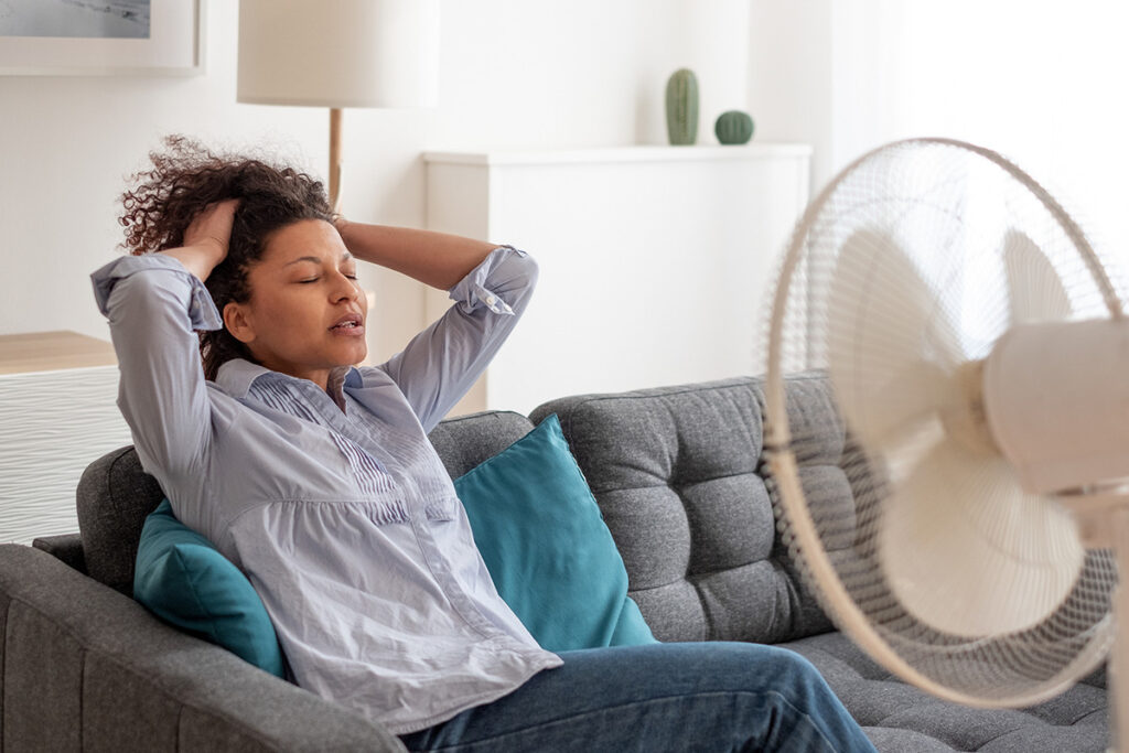 A woman sitting on a couch with a fan blowing on her